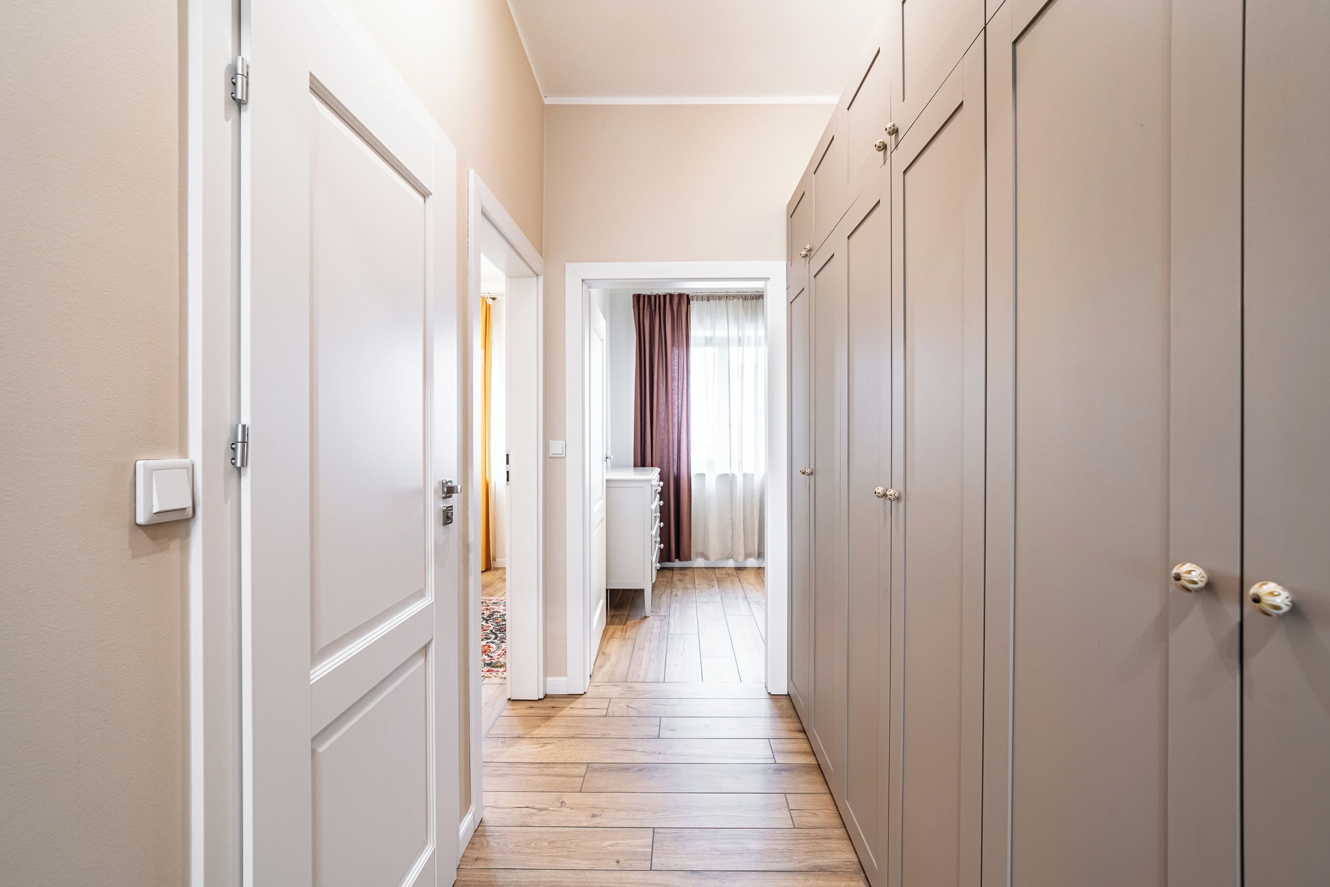 A hallway with a wooden floor, a white door on the left, and a wardrobe on the right.