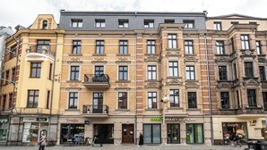Un immeuble à plusieurs étages, doté de nombreux commerces en rez-de-chaussée, notamment une pharmacie et un restaurant.