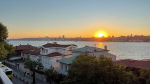 Ein Sonnenuntergang über einem Gewässer, im Vordergrund befinden sich Gebäude.
