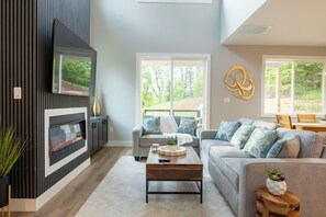 Ein modernes Wohnzimmer mit Kamin, grauen Sofas und Blick ins Freie.