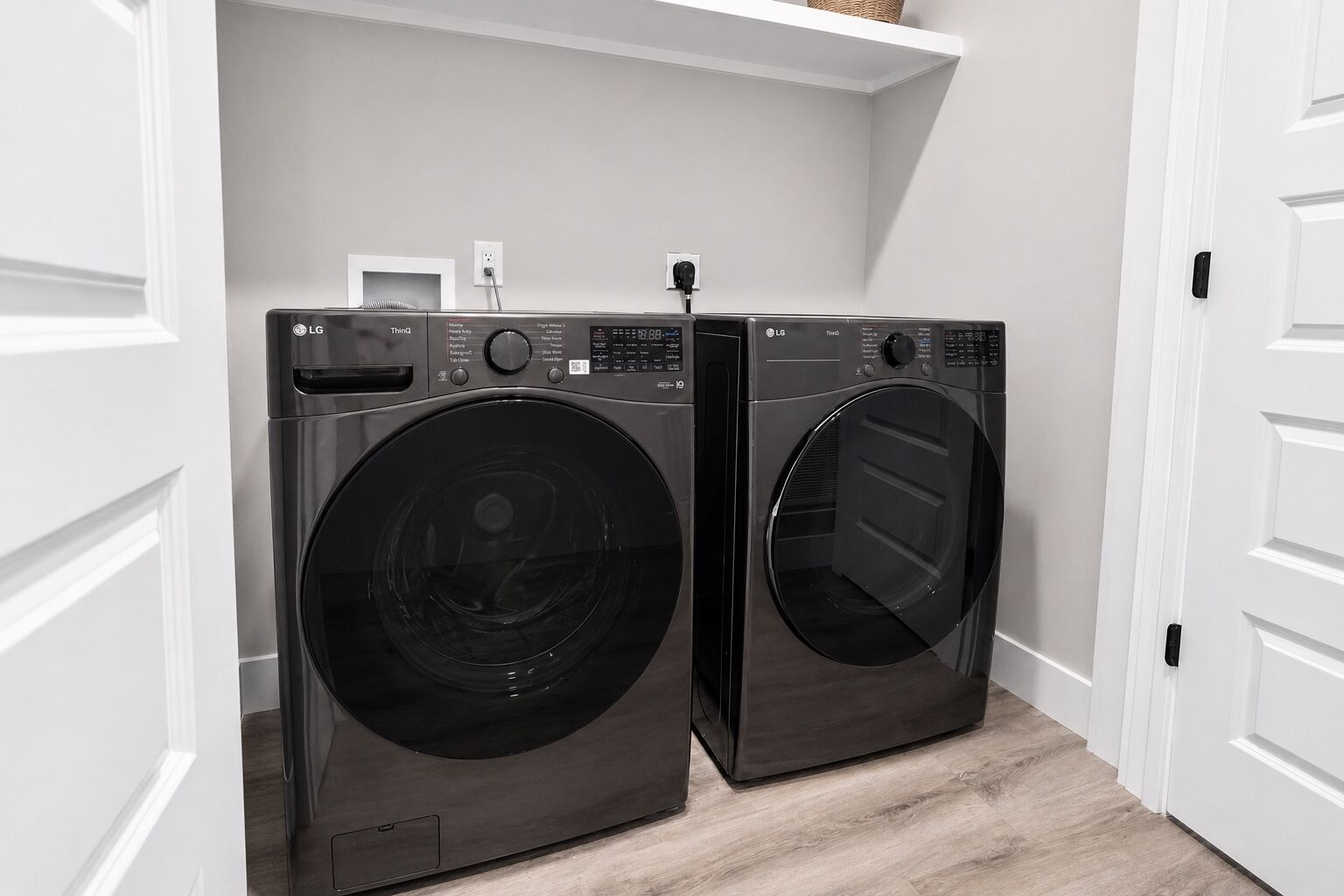 Deux lave-linge LG ThinQ à chargement frontal, dans une buanderie aux murs blancs et au plancher en bois.