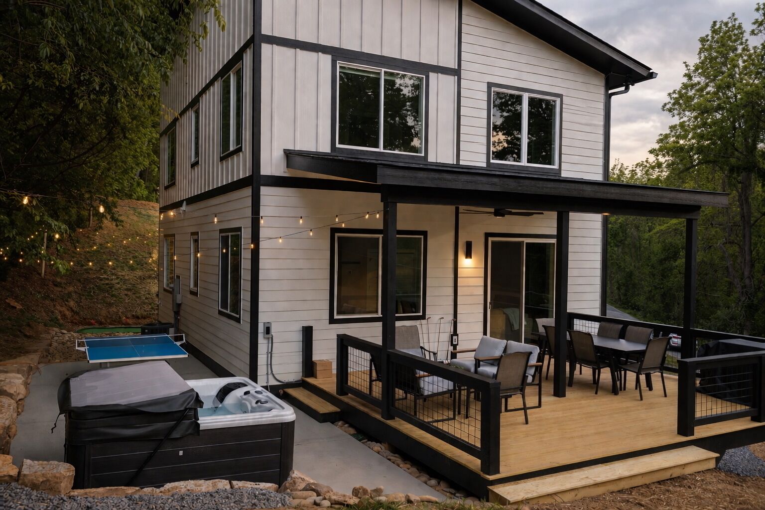 Ein modernes, zweistöckiges Haus mit überdachter Terrasse, Sitzgelegenheit im Freien und einem Whirlpool.