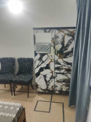 Une pièce comprenant deux chaises de couleur foncée, un meuble orné de motifs et un lit recouvert d’une couvre-lit à motifs.