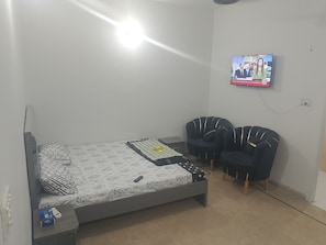 Ein Schlafzimmer mit einem Bett, zwei Stühlen, einem Fernseher und einer Steckdose.