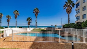 A pool area with a white fence, palm trees, and a building in the background. - 75 Cap D'Azur (Cape Town)