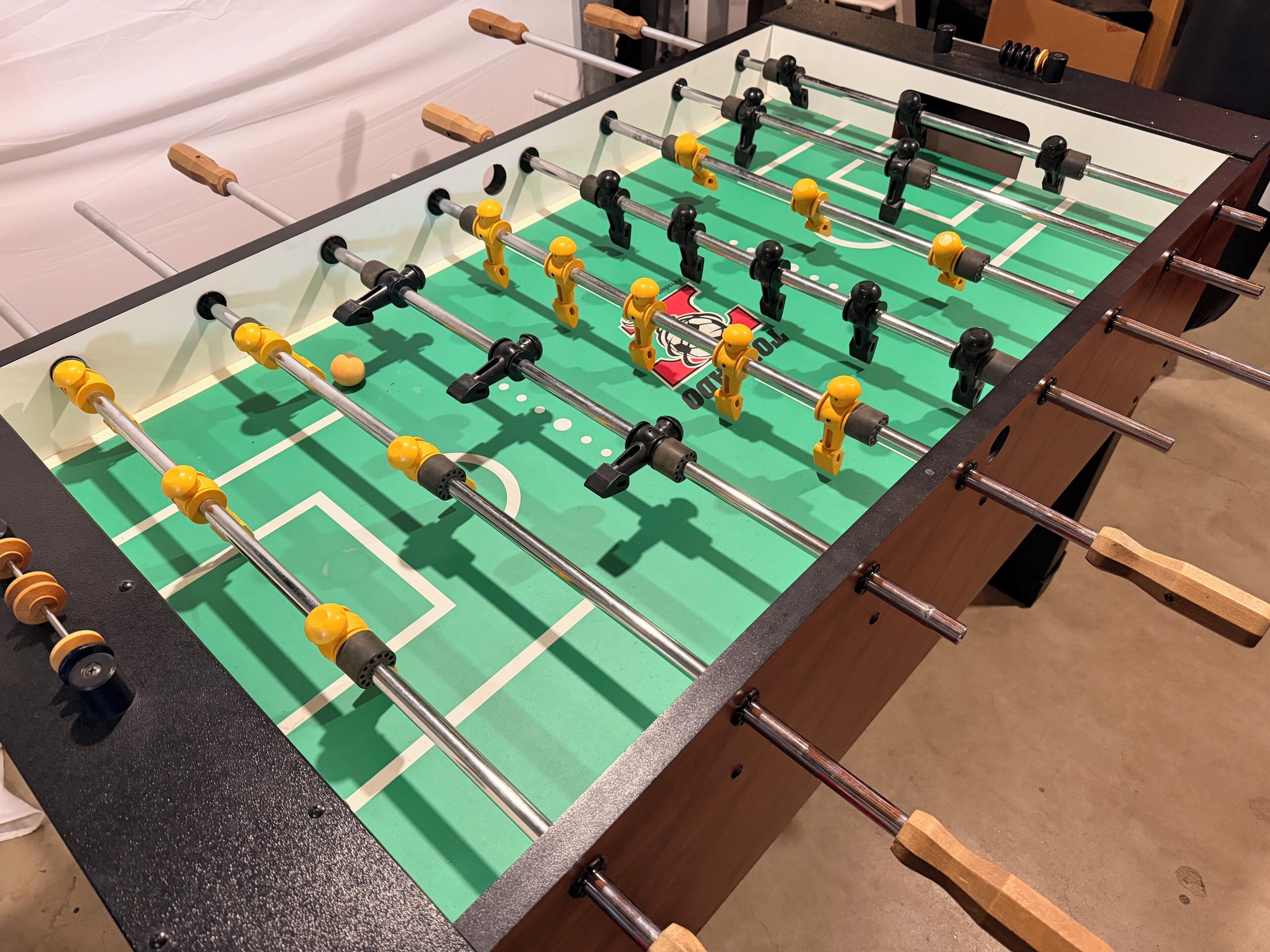 Ein Kicker mit grüner Spielfläche und einem Logo in der Mitte.