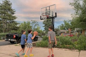 Ein Wohngebiet mit einem Basketballplatz, einem Korb, Bäumen und geparkten Fahrzeugen.