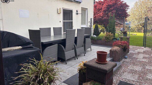 Un patio al aire libre con mesa y sillas, una parrilla cubierta y plantas en macetas.