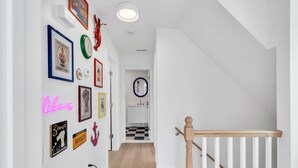 Um corredor com escada, paredes brancas e várias quadros e decorações.