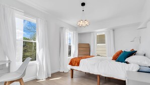 Quarto com cama, mesa de cabeceira, cadeira e janela com cortinas.