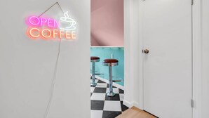 Um corredor com um letreiro de neon que diz 'OPEN COFFEE', uma porta branca e dois banquetes com assentos vermelhos.