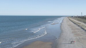 A beach with a long stretch of sand, a few people walking, and a distant view of buildings. - Palmwood Haven (Tybee Island)