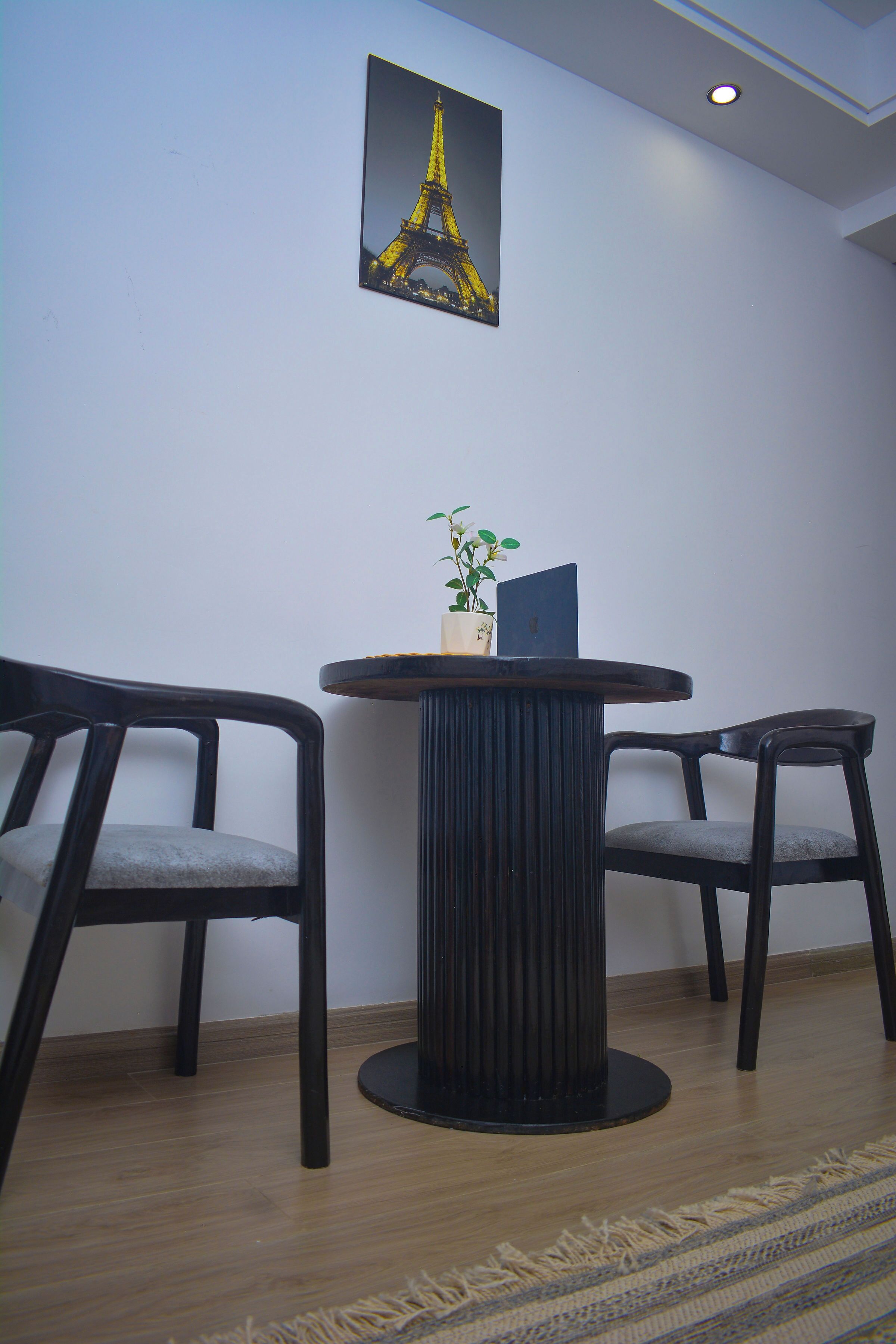 A room with a round table, two chairs, a potted plant, a framed picture of the Eiffel Tower, and a patterned rug.