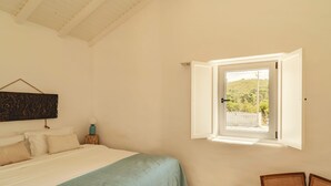 A bedroom with a bed, a window, a chair, and a wall-mounted artwork. - Exclusive Villa Serra de Baixo - Porto Covo (Setúbal)