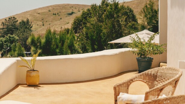 A rooftop terrace with wicker furniture, a potted plant, and a view of a hill. - Exclusive Villa Serra de Baixo - Porto Covo (Setúbal)