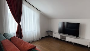 Een moderne woonkamer met een flatscreen televisie, een bank en een raam met dunne gordijnen.