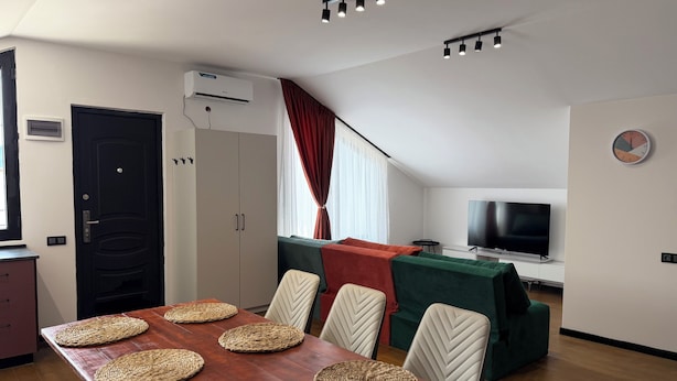 Een moderne kamer met een eettafel, gedekt met placemats, een televisie en een klok aan de muur.