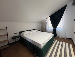 A single bed with a green headboard in a room with a sloped ceiling, a small side table, a black chair, and a striped rug. - Apartment With Terrace (Tbilisi)
