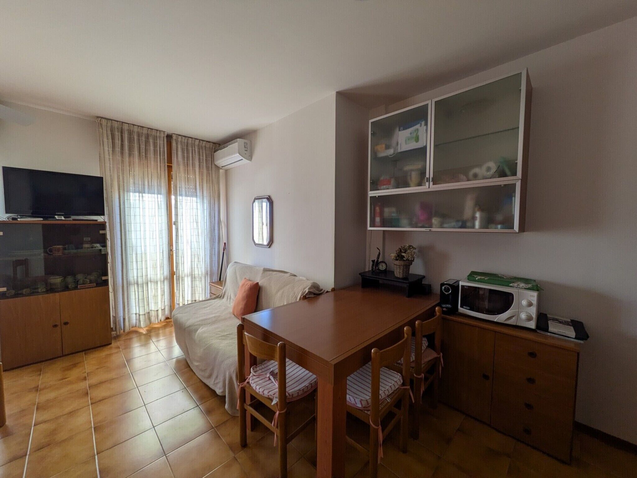 A cozy living room with a sofa, TV, wooden cabinet, and a dining table with chairs.