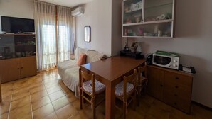 Uma sala de estar aconchegante com sofá, televisão, aparador de madeira e uma mesa de jantar com cadeiras.