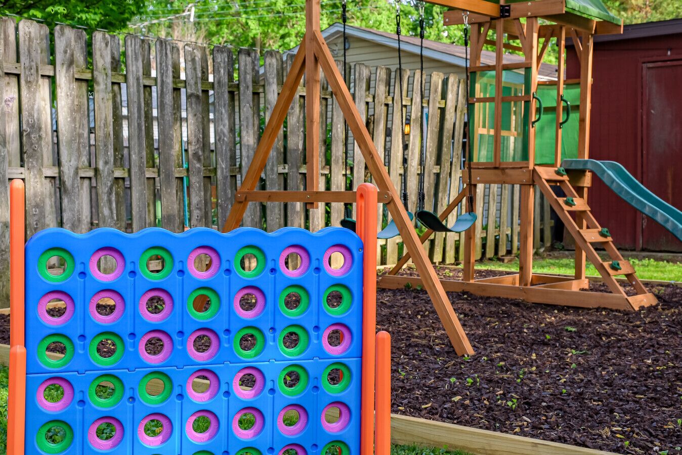 Un terrain de jeux équipé d’une balançoire et d’un toboggan, entouré d’une clôture en bois et agrémenté d’un parterre de fleurs.