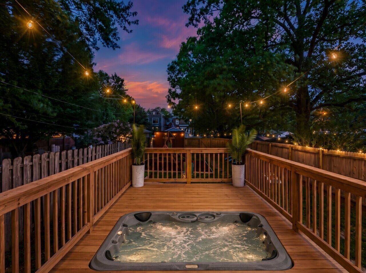 A wooden deck with a hot tub, surrounded by a wooden fence and string lights.