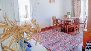 Zona pranzo con tavolo e sedie in legno, un tappeto colorato e una pianta in vaso.