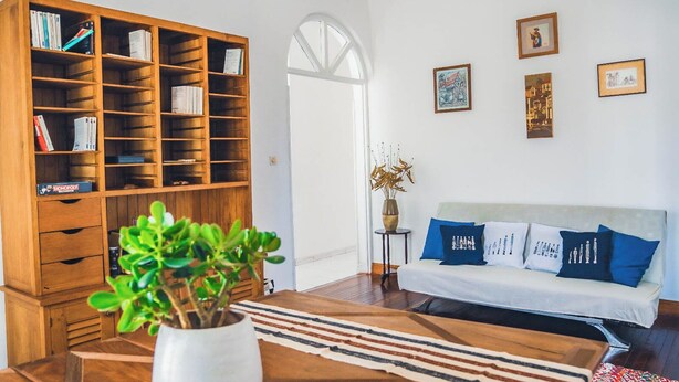 Un soggiorno con una libreria in legno, un divano bianco con cuscini blu e un tavolino da caffè con un tappeto a righe.