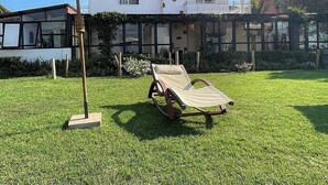 Una casa moderna con facciata bianca, veranda in vetro e prato con una sdraio e un ombrellone.