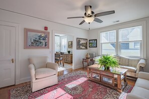 Ein Wohnzimmer mit Deckenventilator, einer Couch, einem Couchtisch und einem großen Fenster mit Jalousien.