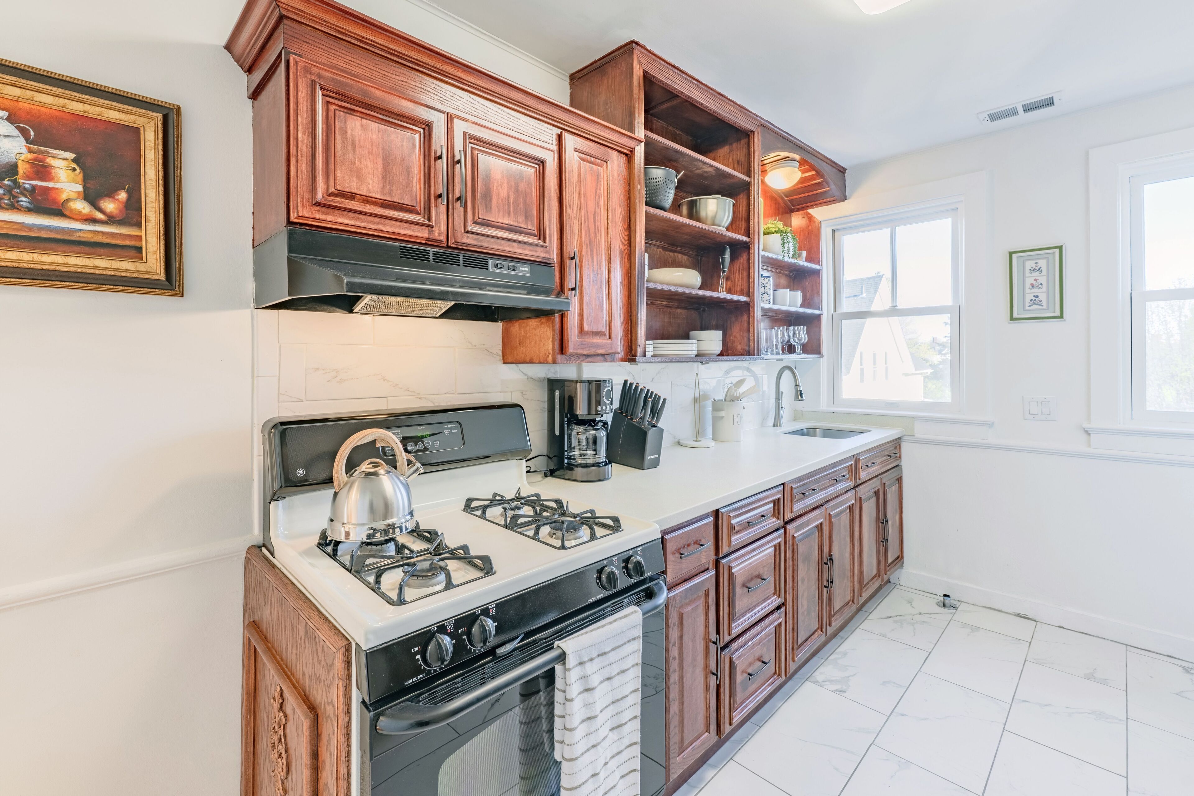 A kitchen with wooden cabinets, a gas stove, a coffee maker, and a window with a view.