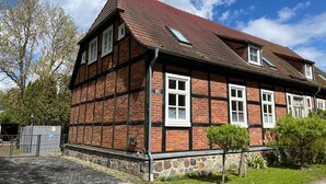A traditional half-timbered building with a sloped roof, a small garden, and a paved entrance.