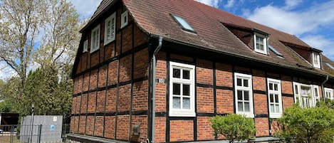 A traditional half-timbered building with a sloped roof, a small garden, and a paved entrance.
