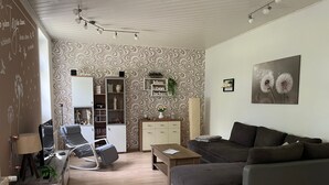 A modern living room with a sofa, a coffee table, a bookshelf, and a desk with a lamp.