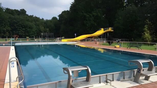 A swimming pool with a slide, surrounded by a brick deck and metal railings.