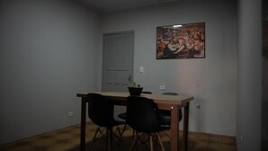 A dining area with a wooden table, two black chairs, a door, and a painting on the wall. - Hostel Estação da XV (Telêmaco Borba)