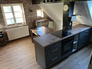 A modern kitchen with a built-in stove, a window, a radiator, and a brick wall. - Holiday Apartment for 5 People (55 m²) in Ivenack (Ivenack)