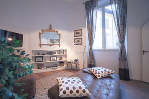A living room with a sofa, a television, a bookshelf, a mirror, and a window with curtains. - Apartments Florence - Pandolfini Suite (Firenze)