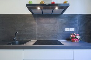 A modern kitchen with a black induction cooktop, a stainless steel sink, and a black range hood. - Apartments Florence - Pandolfini Suite (Firenze)