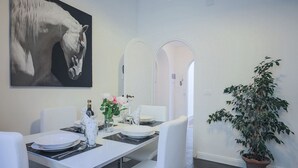 Uma área de refeições com uma mesa branca posta para dois, uma planta em vaso e um quadro grande de cavalos na parede.