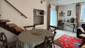 Un coin repas comprenant une table ronde, des chaises, une bibliothèque, un porte-manteau suspendu et une fenêtre avec des rideaux.