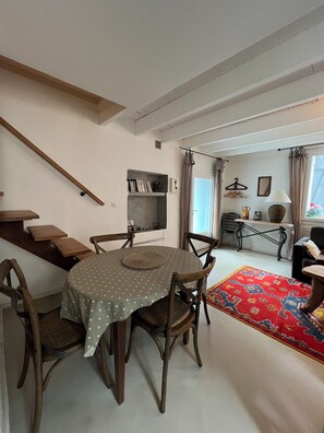 A dining area with a round table, chairs, a bookshelf, a hanging coat rack, and a window with curtains. - La Tannerie, village house in Avène (Avène)