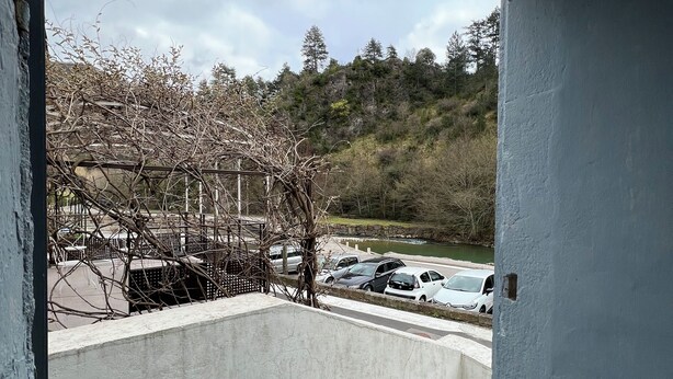 Un balcon donnant sur des voitures garées et un paysage vallonné.