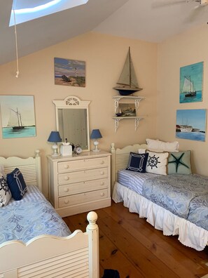 Une chambre avec deux lits, une commode, un miroir et des œuvres d’art murales sur le thème de la marine.