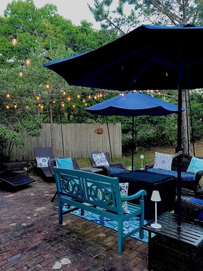 Une terrasse extérieure avec un sol en briques, des meubles de jardin bleus et des guirlandes lumineuses.