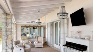 Une pièce comprenant un piano, deux fauteuils, un canapé, un lustre et un téléviseur fixé au mur.