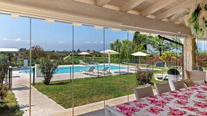 Un espace extérieur abrité comprenant une piscine, des chaises longues et une table recouverte d’une nappe à motifs floraux.