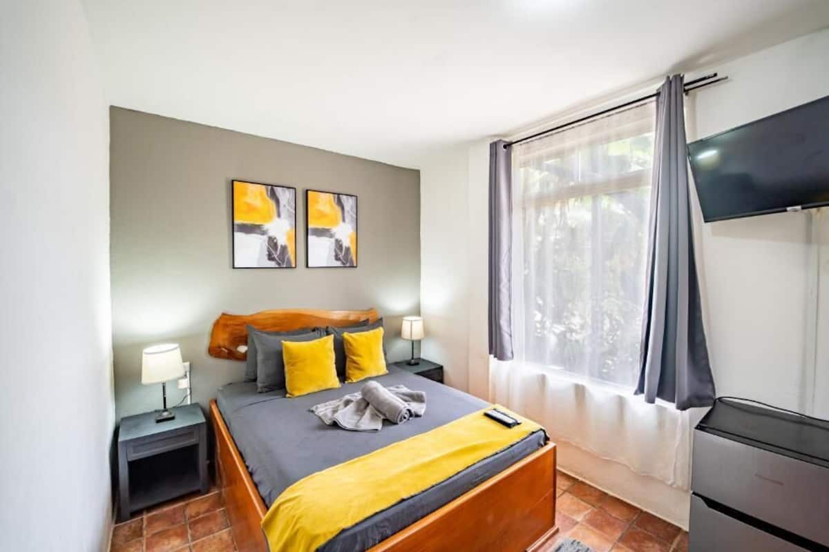 A bedroom with a bed, bedside tables, a TV, and artwork on the wall.
