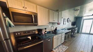A modern kitchen with stainless steel appliances, wooden cabinets, a granite countertop, and a view of the balcony. - Executive Pineapple Escape-Ocean View & Relaxation (Myrtle Beach)