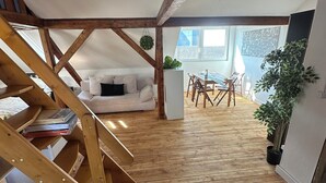 A loft-style room with a wooden staircase, a white sofa, a dining table with chairs, and a potted plant. - Cozy attic apartment main station/city (Nürnberg)